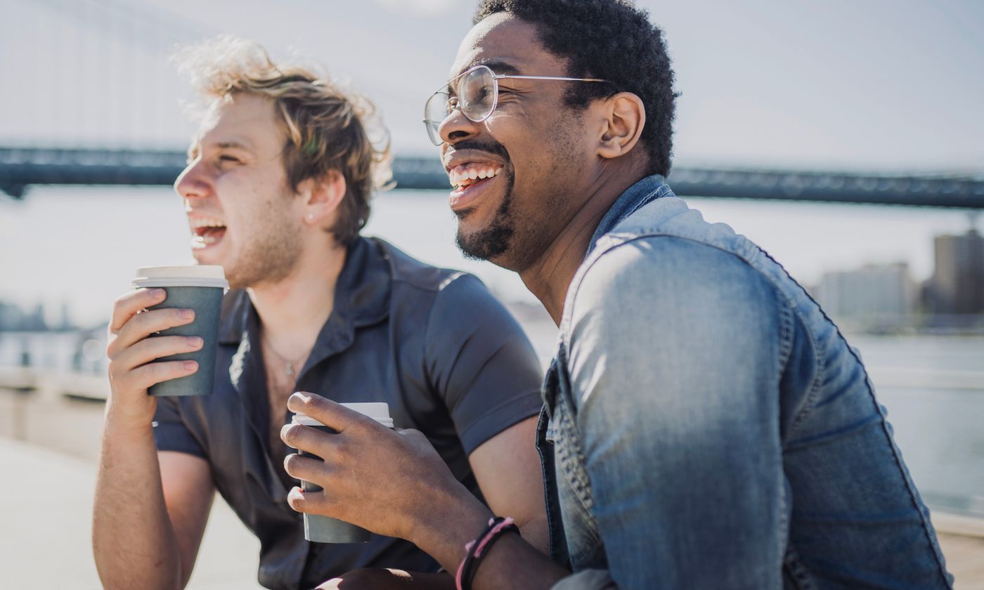 Two friends laughing over coffee beside the water